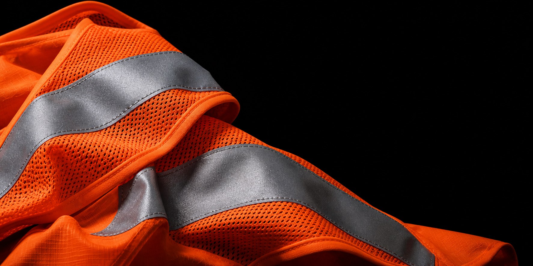 Fluorescent orange technical mesh and silver reflective tape on a black studio background